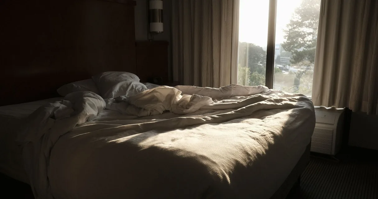Cama desfeita em um quarto com luz da manhã entrando pela janela, ilustrando o cansaço e a queda de libido