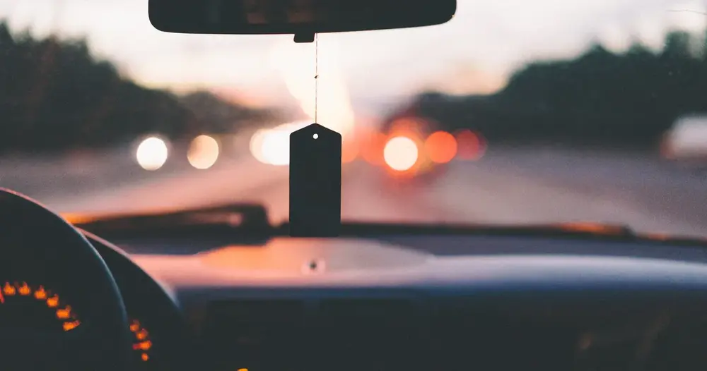 Painel de carro e estrada ao entardecer vistos pelo para-brisa, ilustrando os débitos de veículo no Paraná