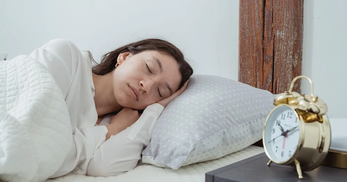 Mulher dormindo de lado em uma cama com despertador ao lado, ilustrando a dor no glúteo ao deitar de lado