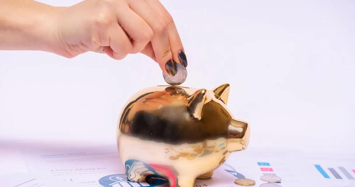 Mão colocando uma moeda em um cofre dourado em formato de porquinho, ilustrando o IPTV barato